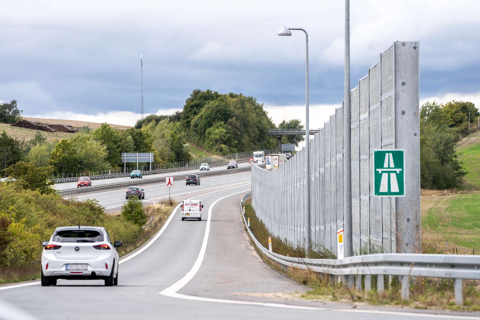 Støjskærm langs med en motorvejstilkørsel, hvor der kører et par biler