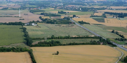 Luftfoto af marker med en vej, der løber igennem og en by i baggrunden