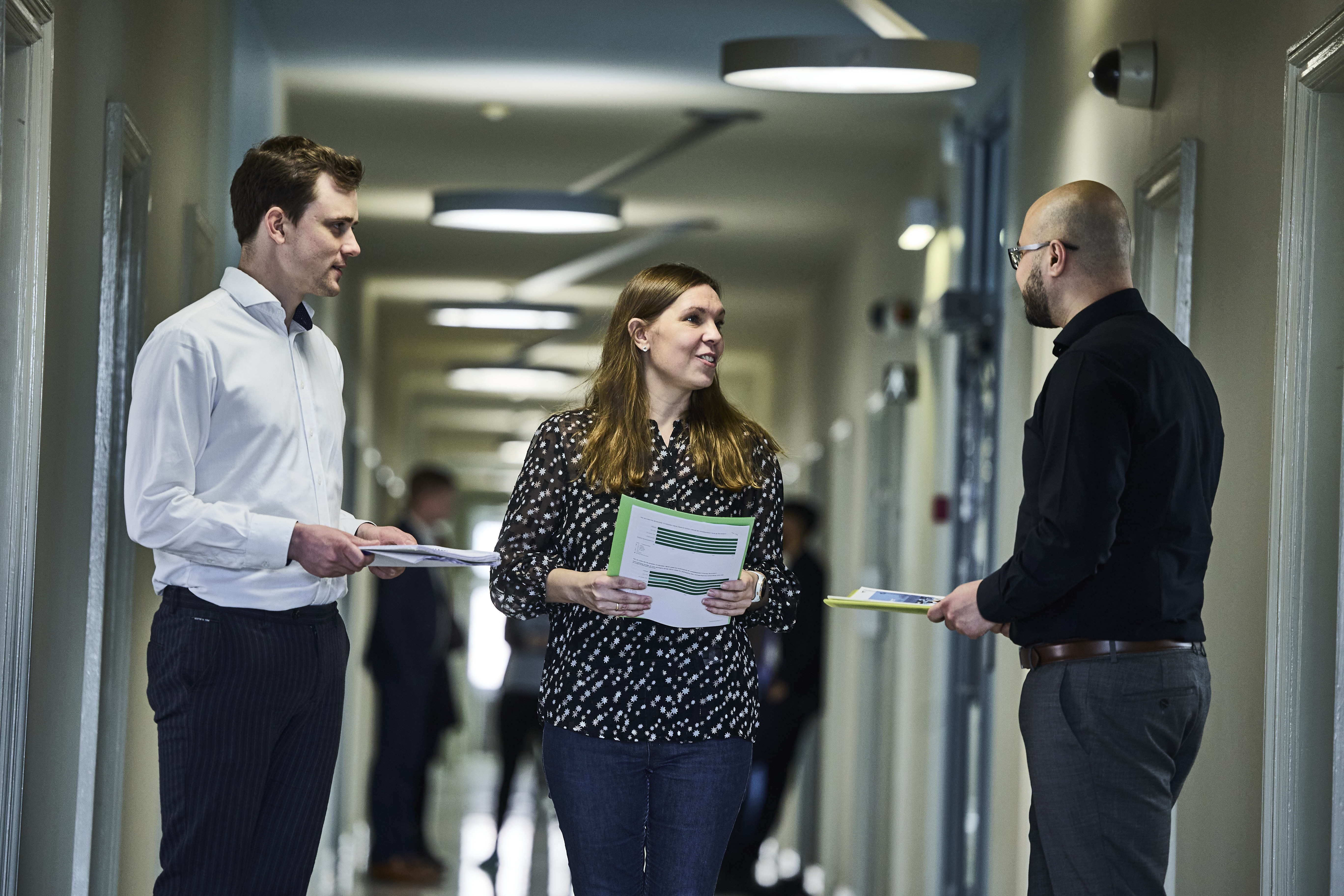 Tre af ministeriets medarbejder taler sammen på gangen i departementet.